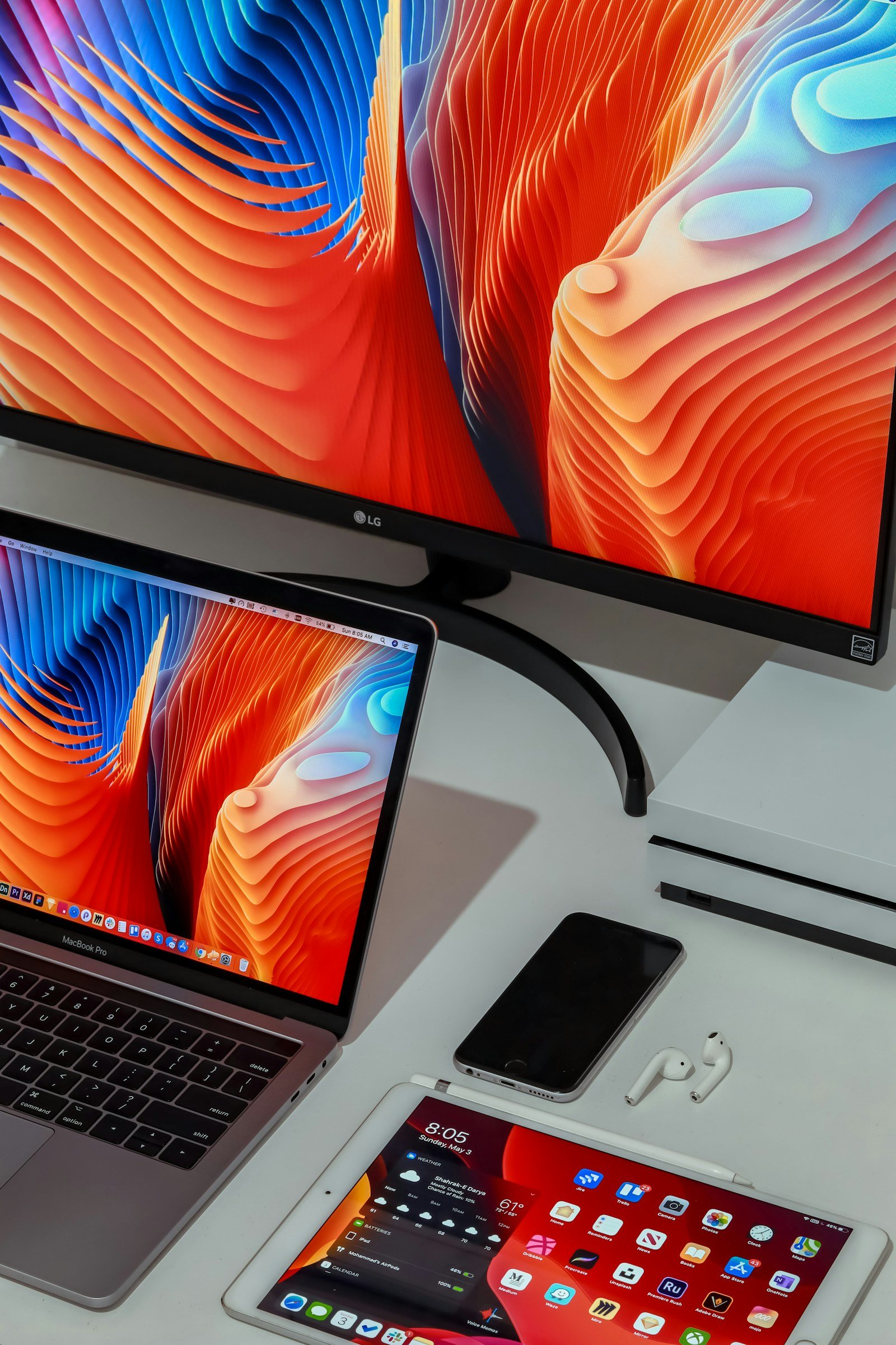 Monitor, laptop, tablet, phone and earbuds on a desk