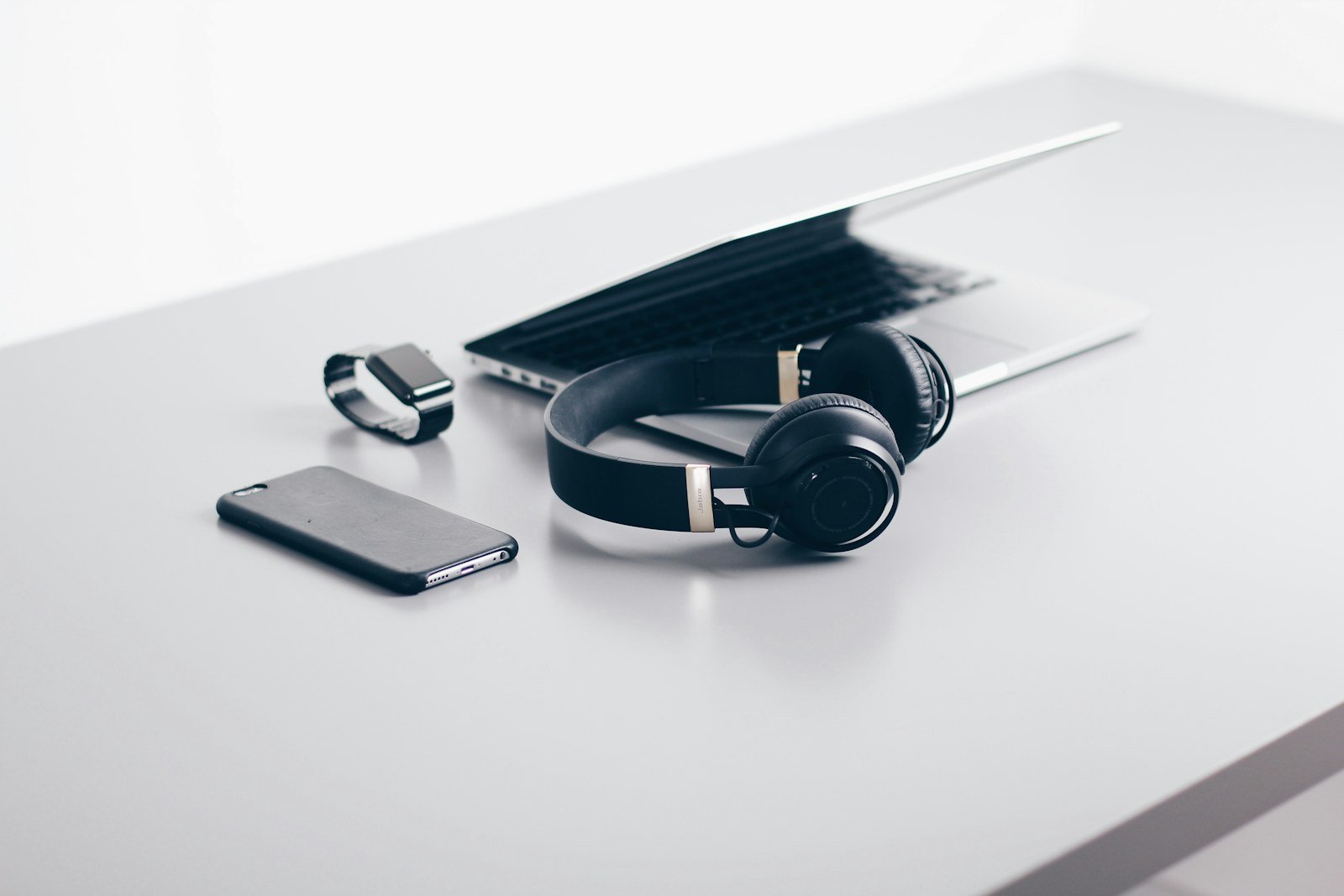 Headphones, smartphone, watch and laptop arranged on a desk
